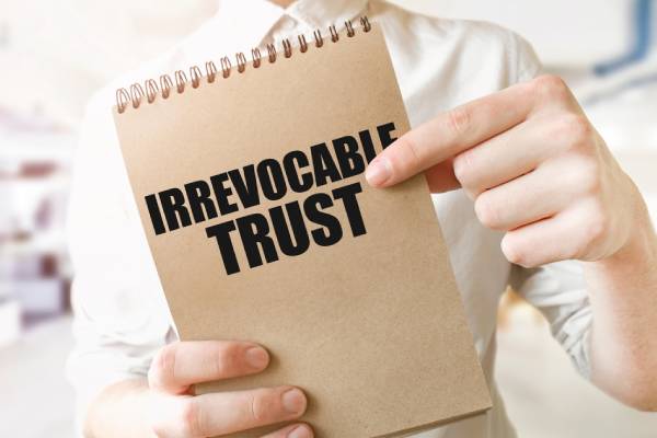 IRREVOCABLE TRUST on brown paper notepad in businessman hands in office.
