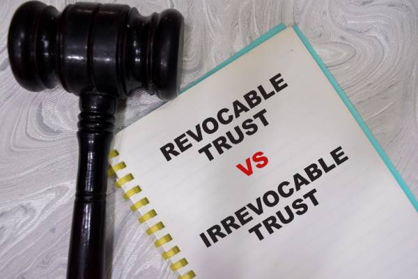 Revocable trust VS irrevocable trust write on book with gavel isolated on Wooden Table.
